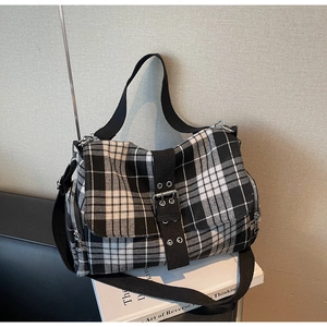 Detail of plaid canvas crossbody bag featuring black webbing strap and silver hardware