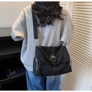 Detailed view of a black canvas crossbody bag featuring flap straps and side zippers