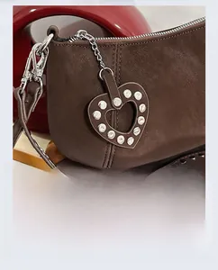 Detail of dark brown lychee leather bag featuring a heart-shaped rhinestone charm and silver studs
