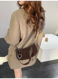 Detail of dark brown crescent bag with silver studs and heart pendant on shoulder