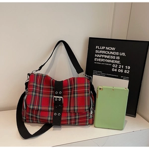 Detail of red plaid shoulder bag with black eyelet straps and silver hardware accents