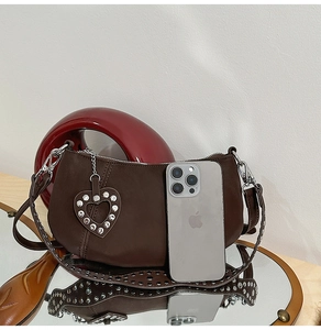 Close-up of a dark brown crescent bag with silver studs and a heart charm