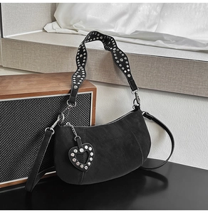 Detail of black matte crescent bag featuring silver rivets and heart charm on wavy strap