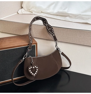 Detail of dark brown leather crescent bag with silver rivet studs and heart pendant charm