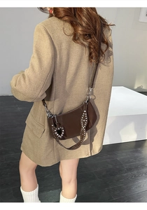Detail of dark brown leather crossbody bag with rivet strap and heart pendant charm