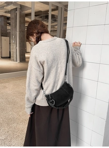 Detail of matte black crescent bag featuring silver rivets and heart charm on a model