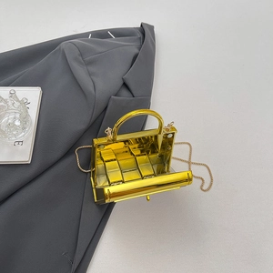 Mini acrylic gold box bag with chain strap and top handle displayed on a stylish suit blazer