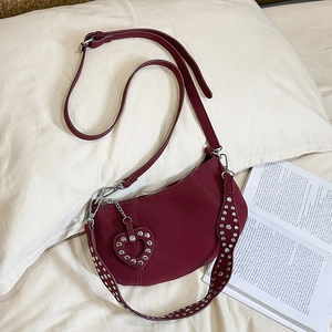 Burgundy crescent shoulder bag with silver studs and heart charm on a soft cushion