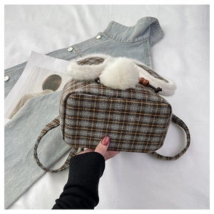 Gros plan d'un sac à dos à carreaux avec oreilles de lapin en peluche et pompon doux