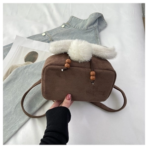 Détail du sac seau en daim marron avec bordure en fausse fourrure blanche et pompons