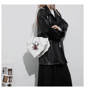 Detail of white heart-shaped bag with black spider web pattern and rhinestone spider
