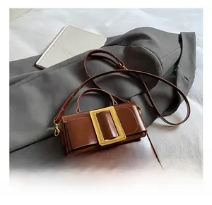 Detail of a brown leather bag featuring a large golden metal buckle and smooth finish