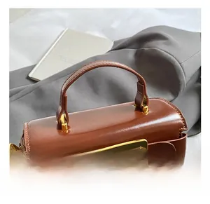 Detail showing the polished brown leather surface and gold square buckle of the handbag
