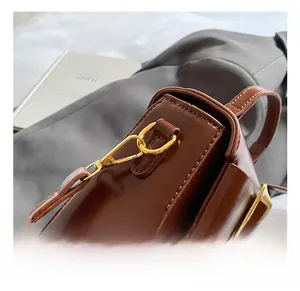 Detail shot of the polished gold metal hook and leather texture on a dark brown handbag