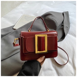 Détail du sac à main rouge vin structuré avec boucle rectangulaire dorée sur tissu