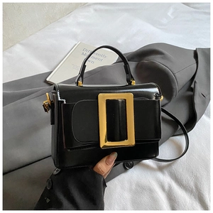 Détail d'un sac à main noir brillant avec une boucle carrée dorée et une poignée simple