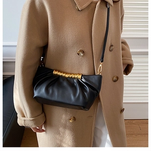 Detail of black pleated cloud bag featuring a unique gold spiral metal handle and leather strap