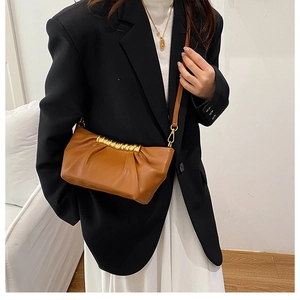 Close-up of brown pleated cloud bag with golden metal bar and slim leather shoulder strap