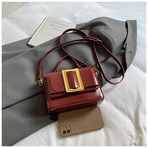 Détail d'un sac bandoulière bordeaux avec boucle dorée posé sur une veste de costume grise