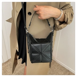 Detail view of black geometric patchwork bucket bag worn with a khaki trench coat