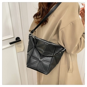 Detail of black geometric bucket bag with triangular panels worn by model in beige coat