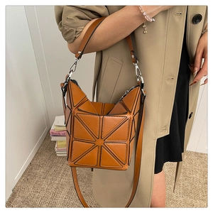 Caramel geometric bucket bag worn by model with beige coat showing casual street style