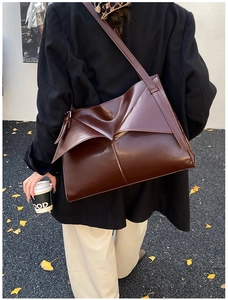 Dettaglio di una borsa tote in pelle lucida marrone scuro con design geometrico a pieghe