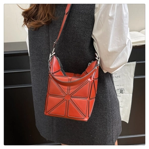 Detail showing orange geometric paneled bucket bag with shoulder strap worn by model