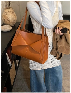 Dettaglio della borsa tote in pelle marrone con piega geometrica portata a spalla
