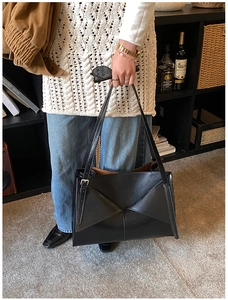 Dettaglio della borsa tote in pelle nera con piega geometrica e fibbia argentata sul manico