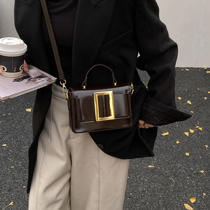 Sac à main minimaliste en cuir marron foncé avec boucle dorée porté par mannequin