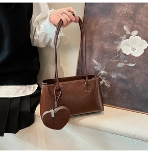 Detail of brown glossy tote bag with matching heart-shaped charm and slim shoulder straps