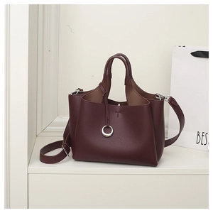Detail of wine red lychee grain leather handbag with accordion side folds and silver charm