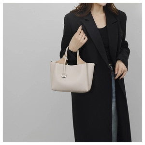 Détail d'un sac seau en cuir beige avec anneau argenté porté par un mannequin femme