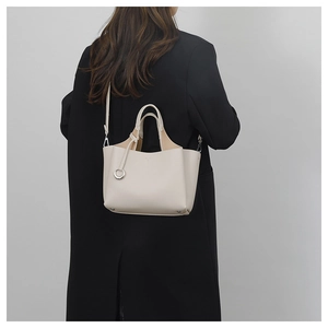 Detail of cream white pebbled leather crossbody bucket bag worn by a model in black coat