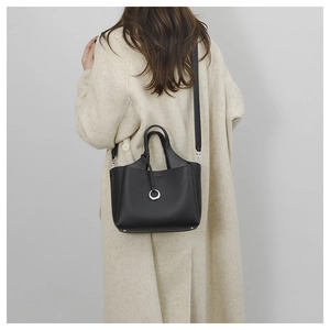 Model wearing a black pebble leather bucket bag with silver ring over an off-white coat