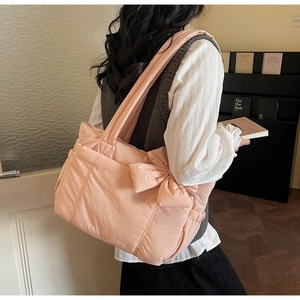 Side view of a pink quilted puffer tote bag with a 3D bow on model's shoulder