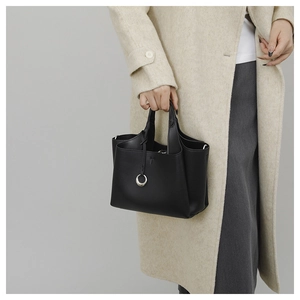 Détail du sac cabas en cuir grainé noir avec anneau argenté sur un manteau beige