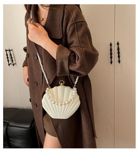 Detail of creamy shell evening bag with pearl handle and metal clasp worn by model
