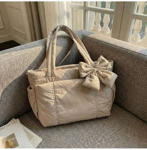 Detail of beige quilted tote bag with large bow on a sofa by the window