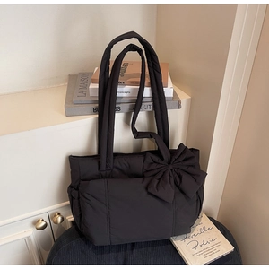 Close-up of a large black quilted tote bag with a decorative side bow on a chair