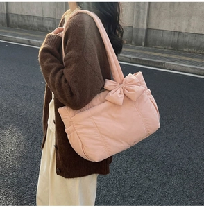 Puffy pink quilted tote bag with a large bow shown on a shoulder in a street setting