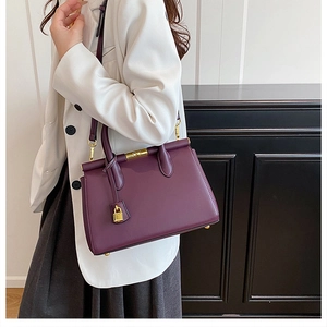 Detail of dark purple leather handbag with gold metal lock and hardware in a professional setting