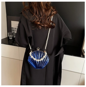 Detail of blue shell-shaped acrylic bag with large pearl handle on a female model