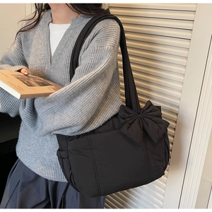 Detail of black quilted tote bag with large bow decoration and padded shoulder strap