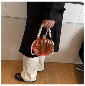 Macro view of shell-shaped orange acrylic handbag with pearl handle and ribbed texture