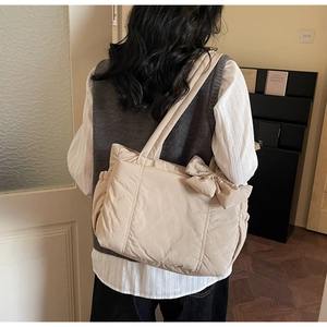 Side view of cream quilted tote bag with large decorative bow on wide shoulder strap