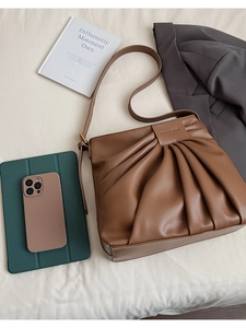Detail view of brown pleated tote bag with brand label and smooth faux leather texture