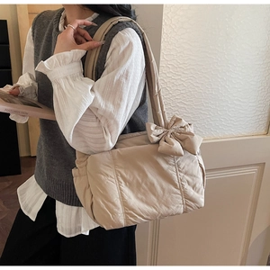 Detail of a beige quilted puffer tote bag with a large decorative shoulder bow strap