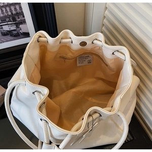 Interior view of white drawstring bucket bag showing orange lining and zipper pocket